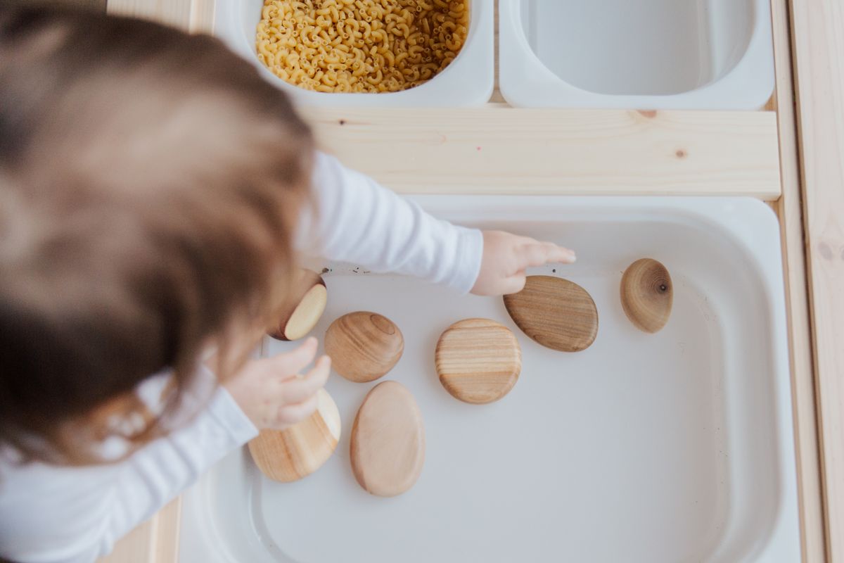 A young child's hands transferring small stones — early fine-motor practical work
